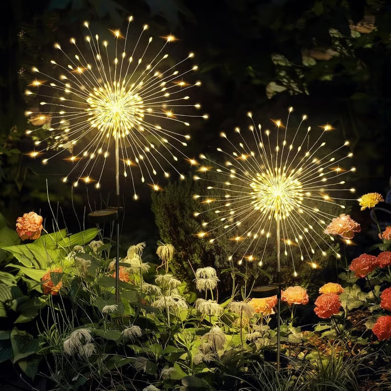 Dos luces solares decorativas tipo fuego artificial encendidas entre plantas